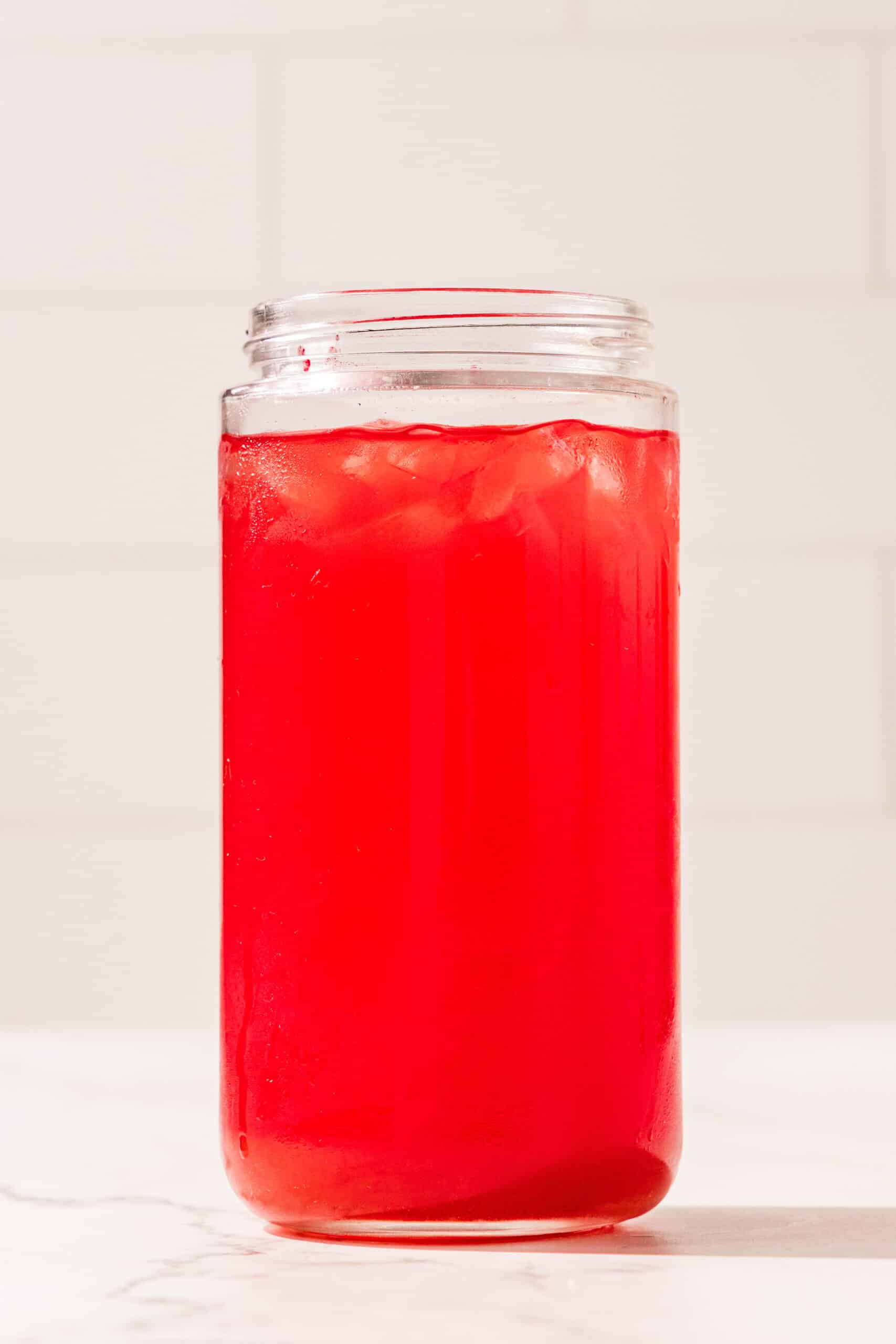 A glass jar filled with red juice and ice.