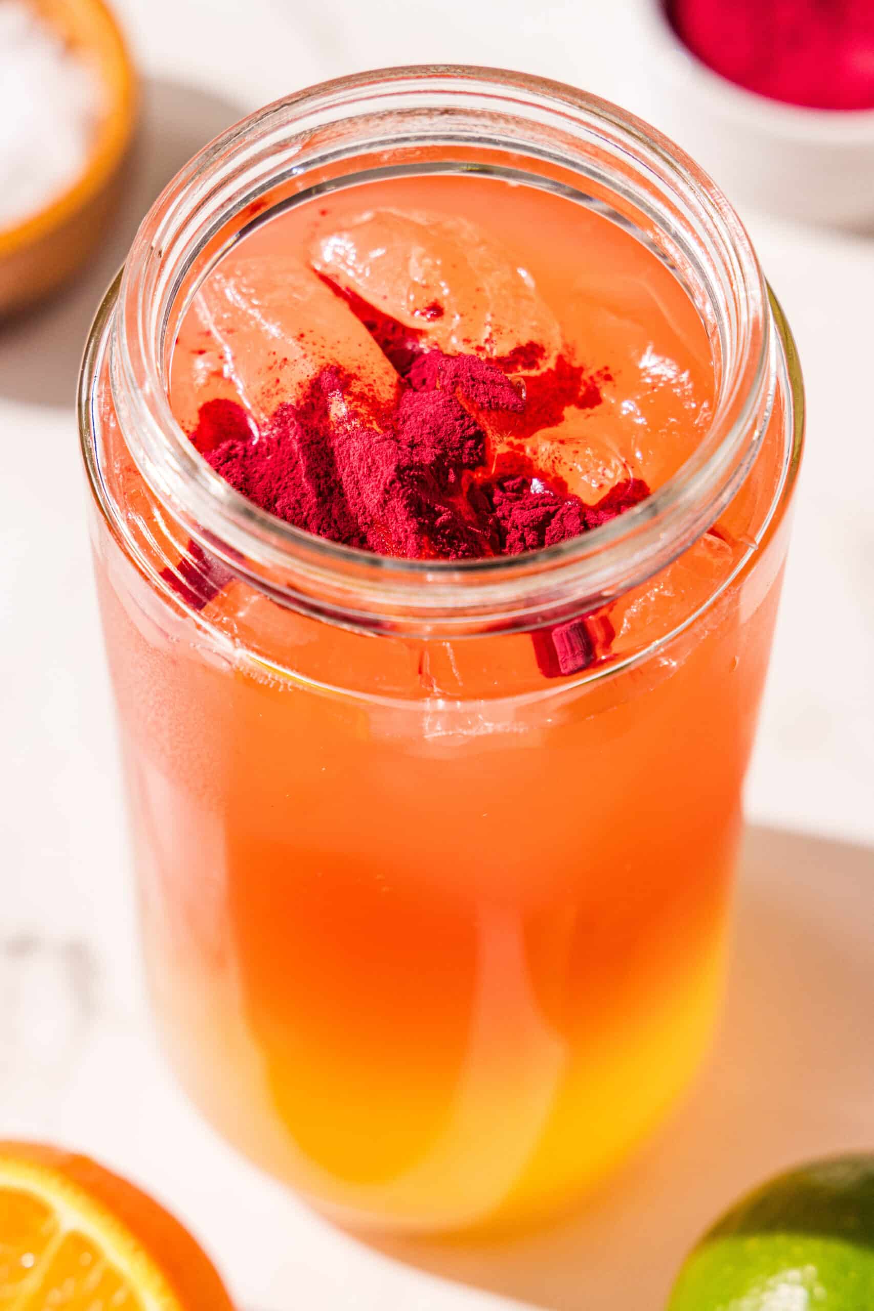 A glass jar filled with orange juice, watermelon juice, and ice and topped with a scoop of beet powder.