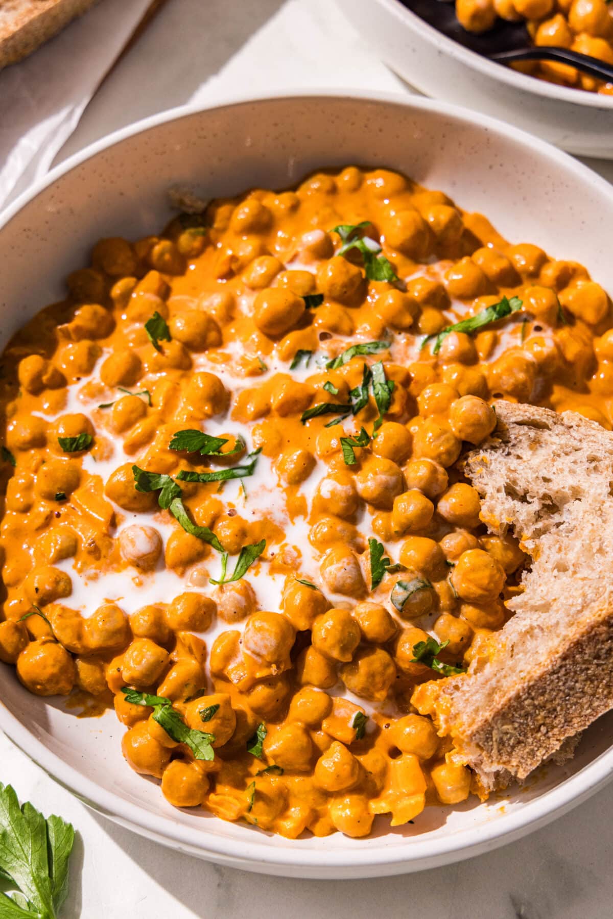 A bowl of curry chickpeas topped with coconut cream and fresh cilantro and a piece of bread dipped in it.