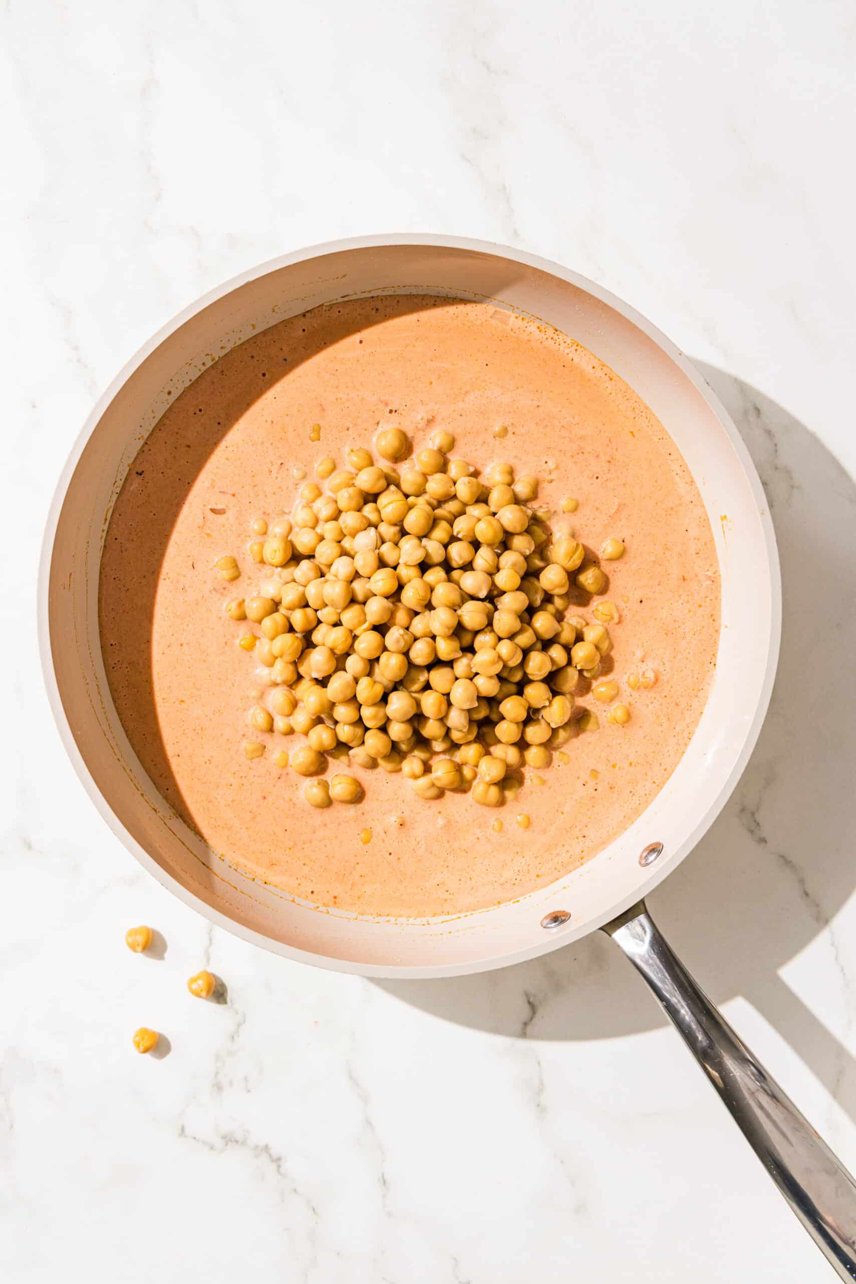 A small frying pan with chickpeas in a curry sauce.