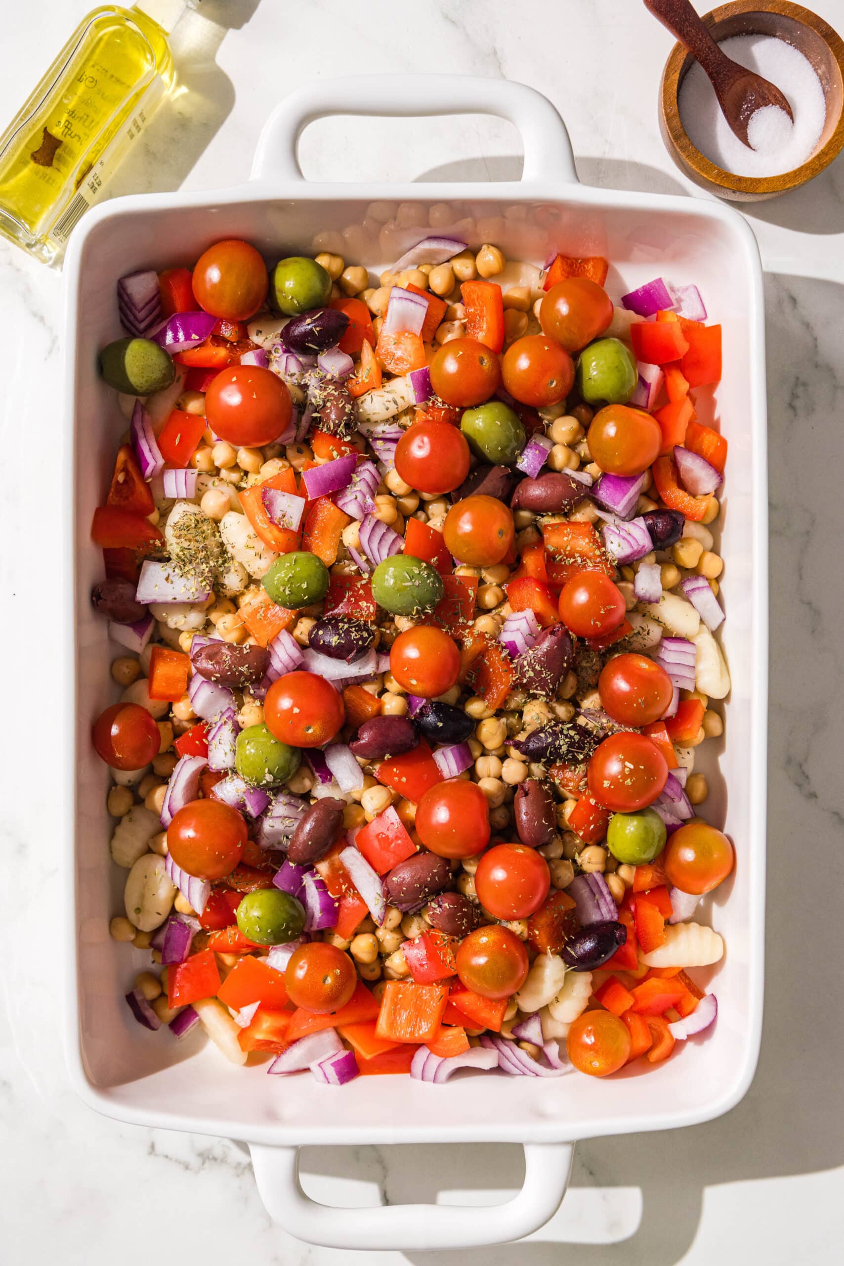A casserole dish filled with gnocchi, chickpeas, chopped bell pepper and onion, cherry tomatoes, and olives.