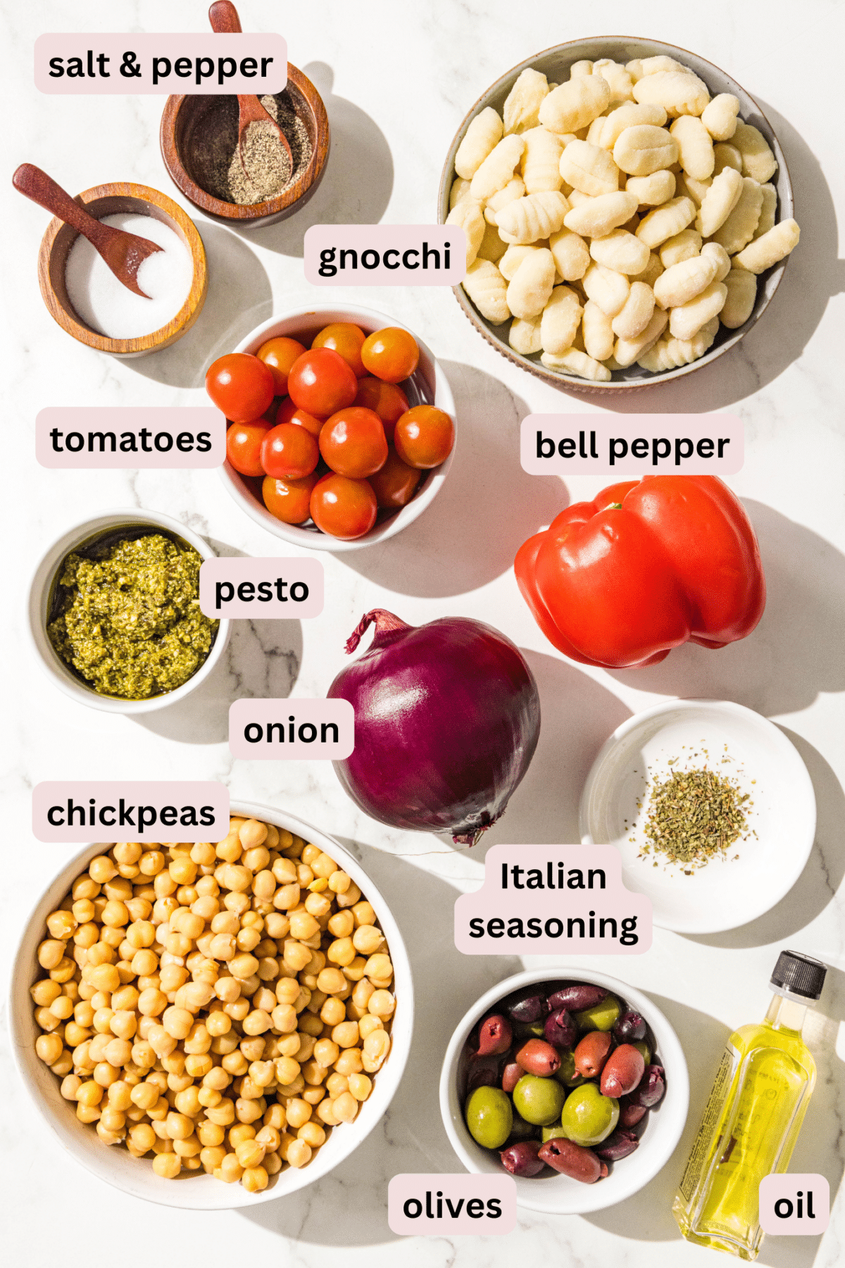 Ingredients in bowls and labeled including: salt and pepper, gnocchi, bell pepper, cherry tomatoes, onion, pesto, Italian seasoning, chickpeas, oil, and olives.