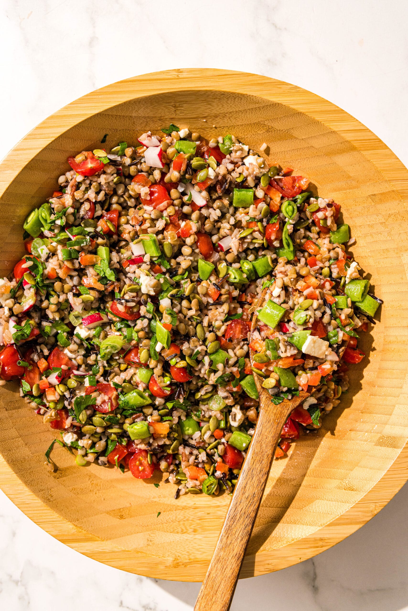A wooden salad bowl of chopped lentil salad and a wooden spoon.