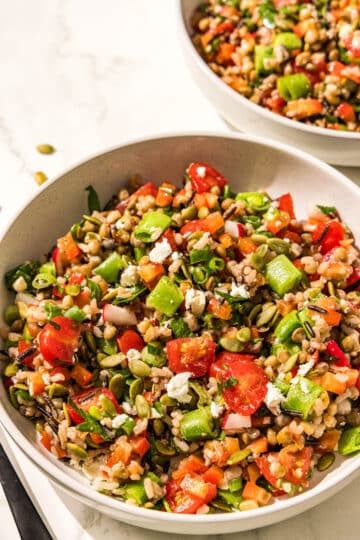 Two bowls of lentil chopped salad and a black metal fork.