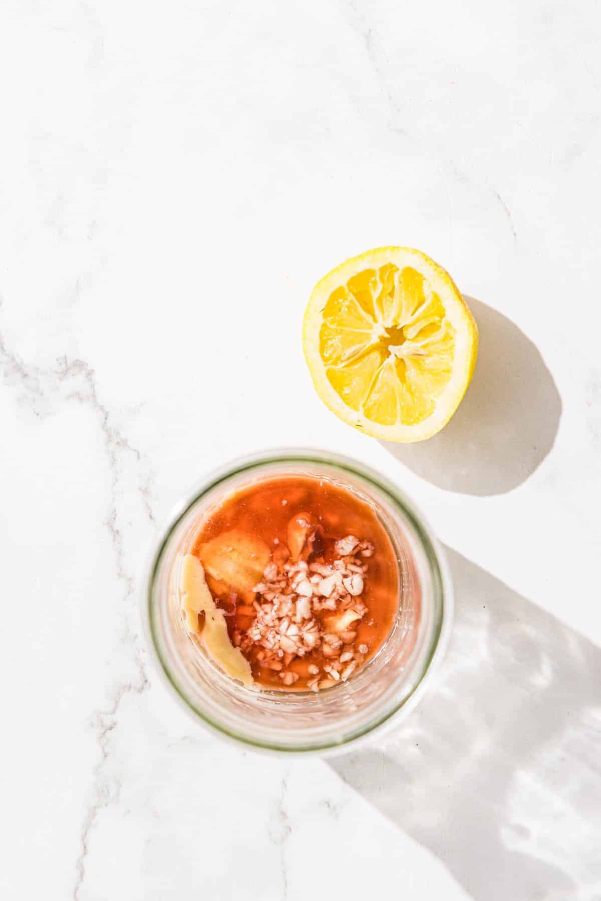 A glass jar filled with tahini, red wine vinegar, and herbs and half of a lemon.