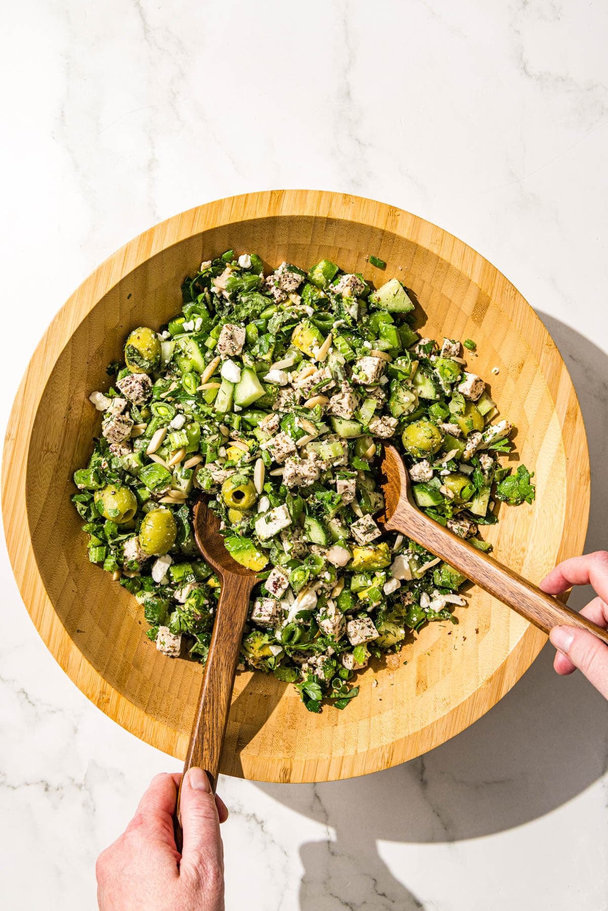 A wooden salad bowl filled with green girl crunch salad and a set of wooden tongs in the bowl.