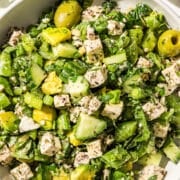 A big bowl of green girl crunch salad with olives, avocado, tofu, herbs, celery, green onion, and snap peas.