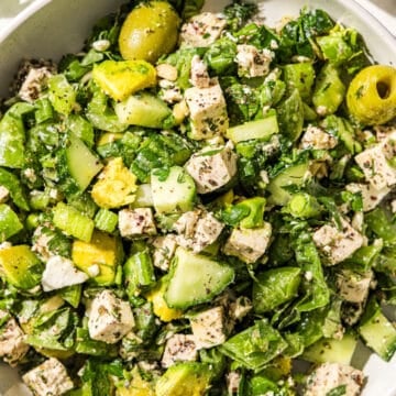 A big bowl of green girl crunch salad with olives, avocado, tofu, herbs, celery, green onion, and snap peas.