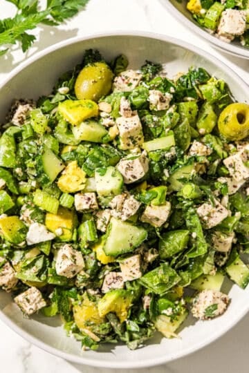A big bowl of green girl crunch salad with olives, avocado, tofu, herbs, celery, green onion, and snap peas.