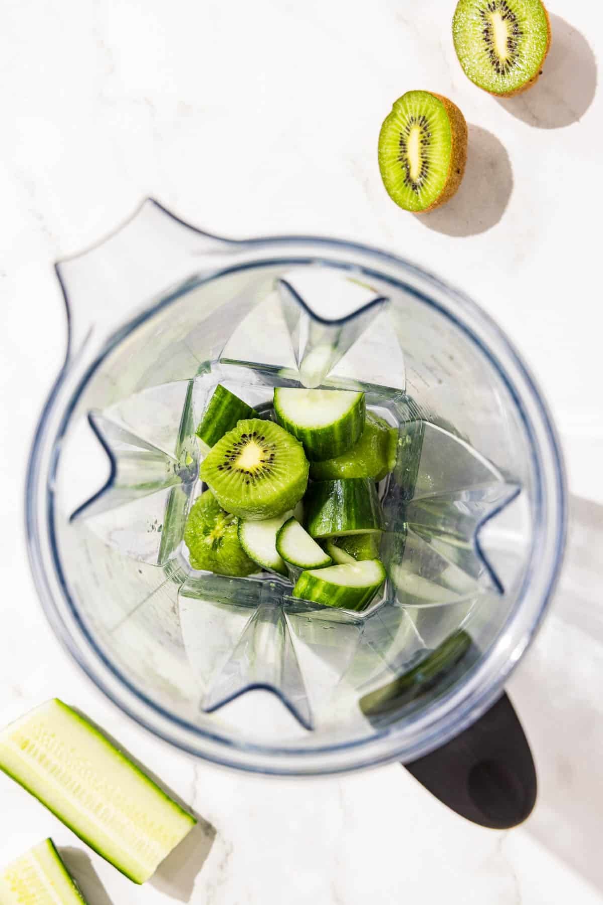 A blender filled with kiwi, cucumber, and lime.