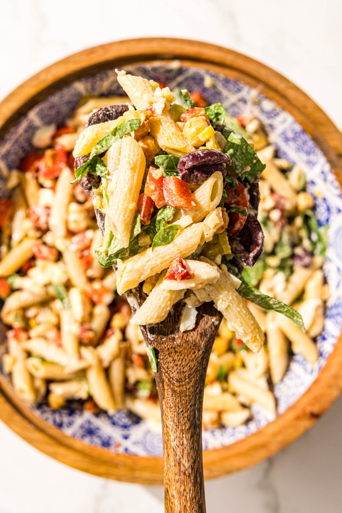 A wooden bowl filled with pasta salad and a wooden spoon holding a scoop of pasta salad.