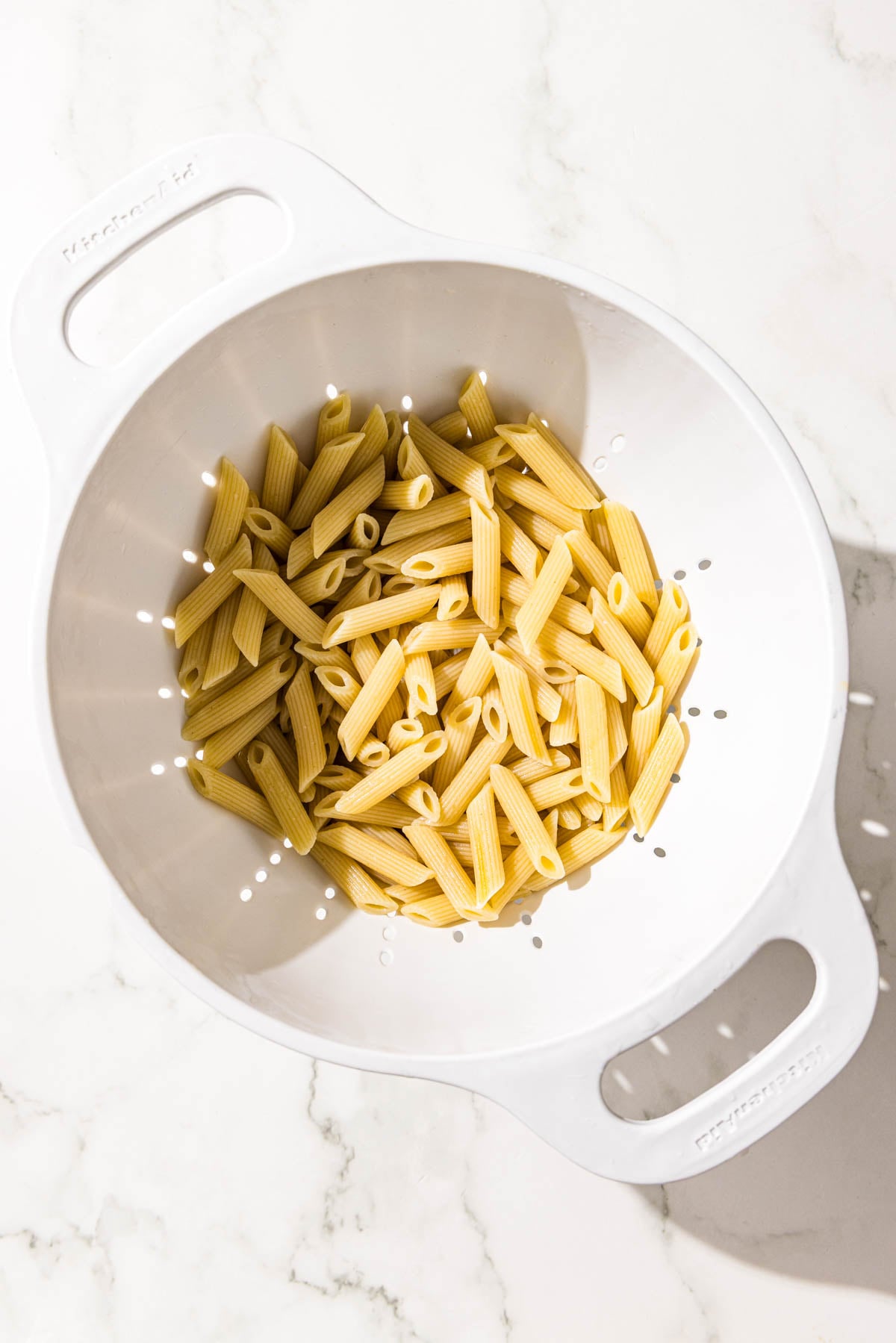 A white colander filled with cooked penne noodles.