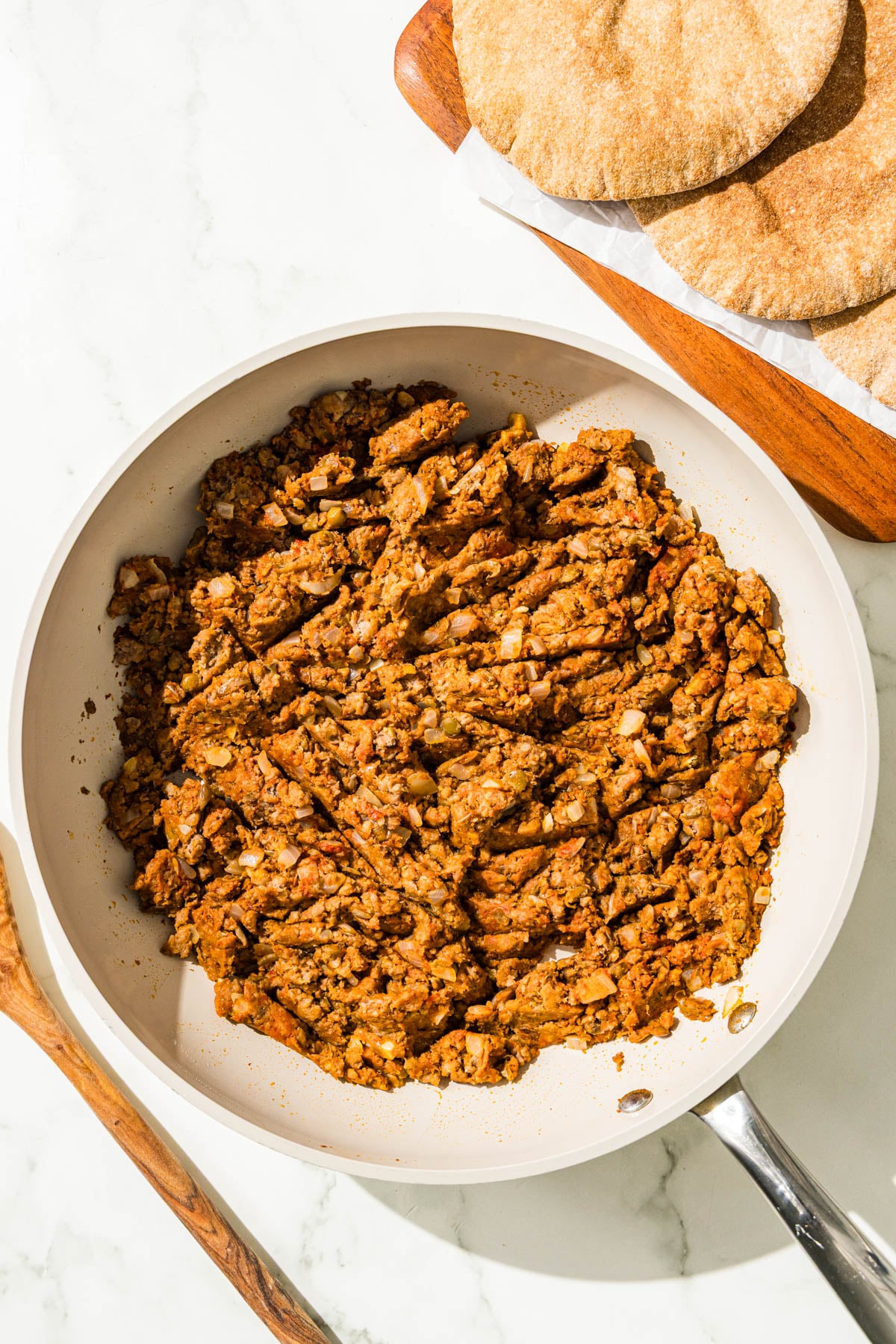 A meaty ground beef lentil mixture in a pan and a stack of three pitas.