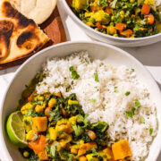 Two bowls of sweet potato curry & rice and a wooden cutting board with toasted naan on it.