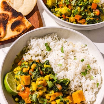 Two bowls of sweet potato curry & rice and a wooden cutting board with toasted naan on it.