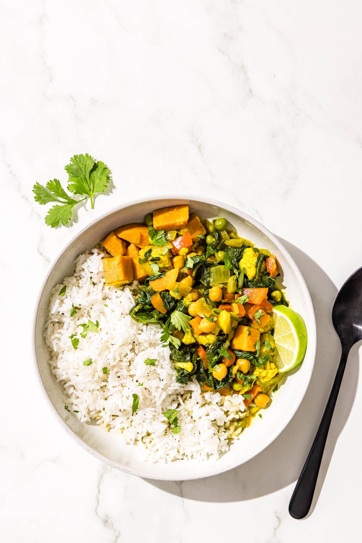 A bowl of white rice and sweet potato chickpea curry and a black metal spoon.