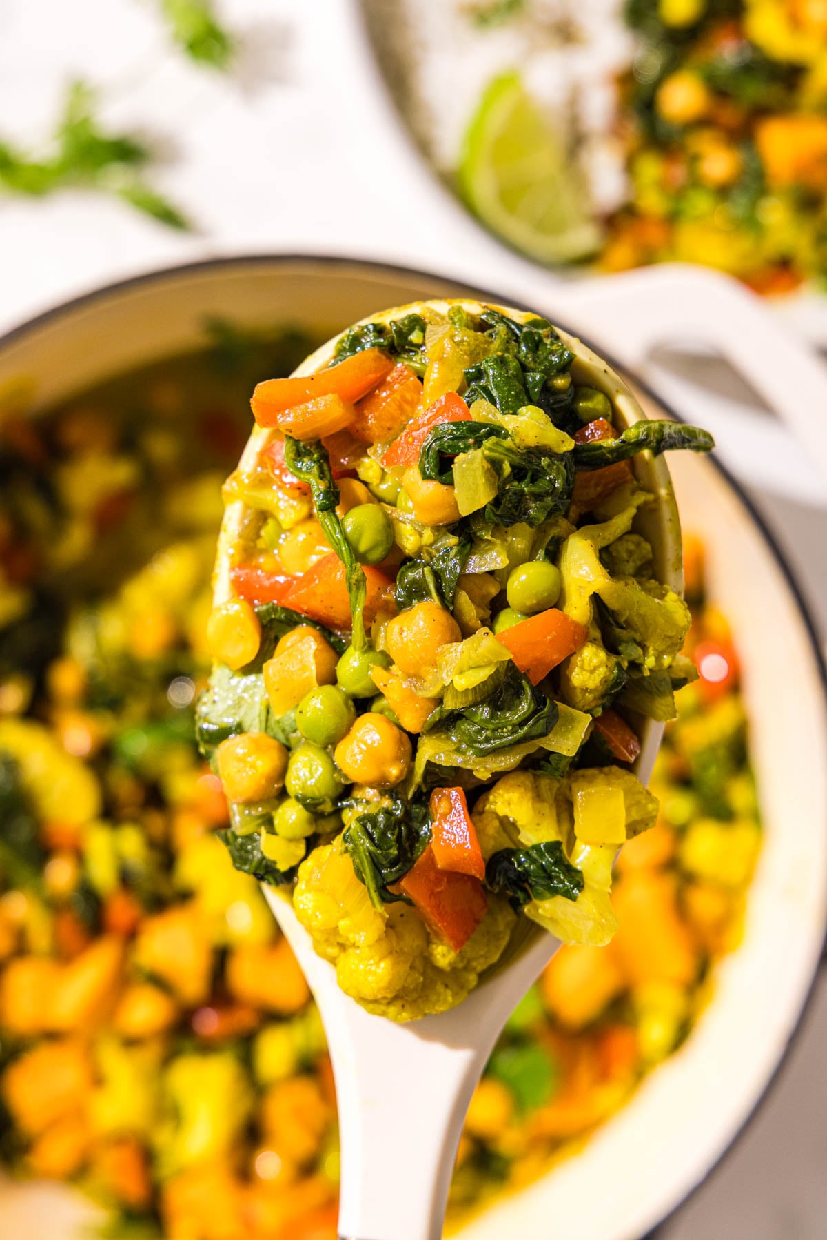 A spoon of sweet potato chickpea curry over a pot of curry.