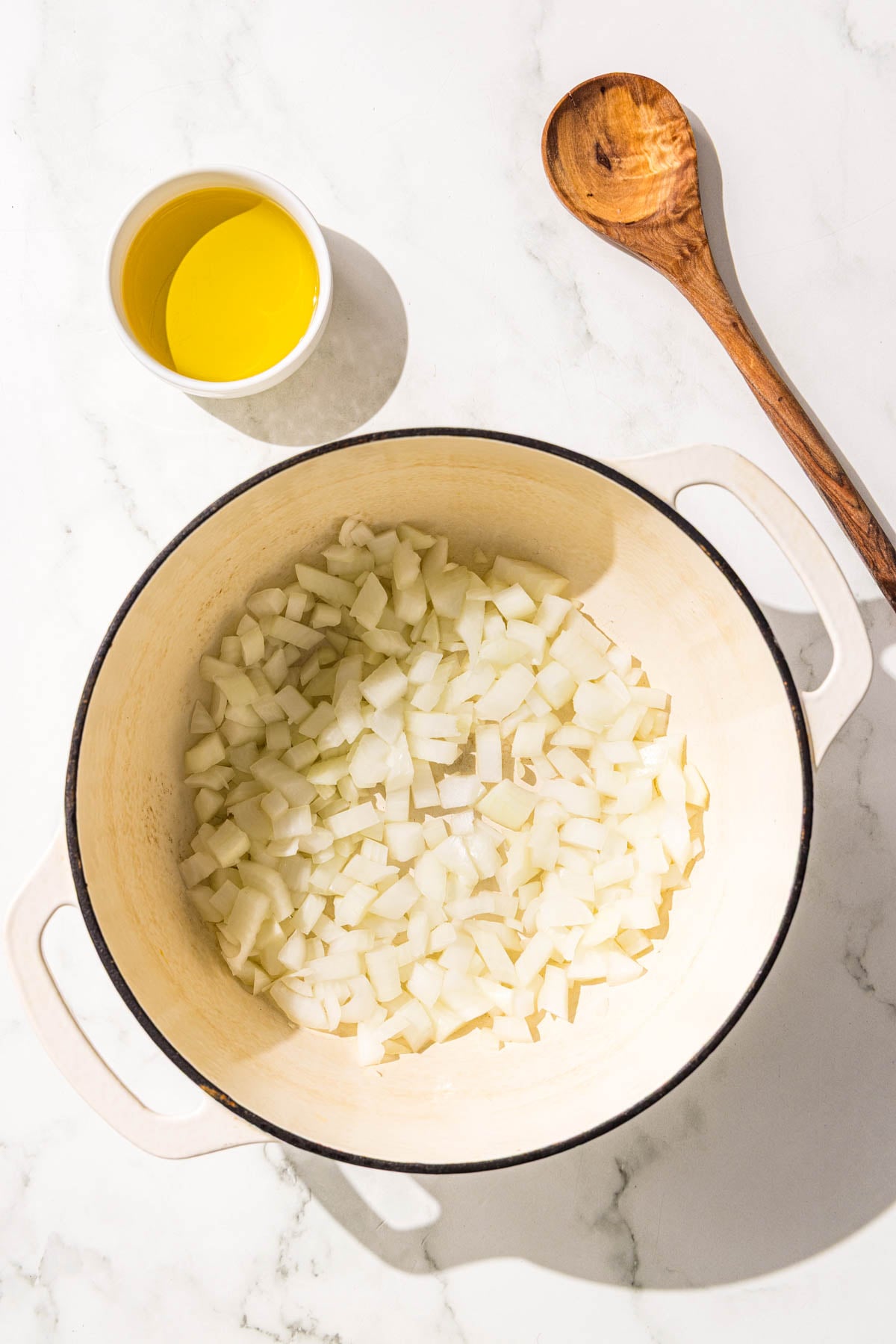 A large pot filled with diced onion, a small bowl of oil, and a wooden spoon.