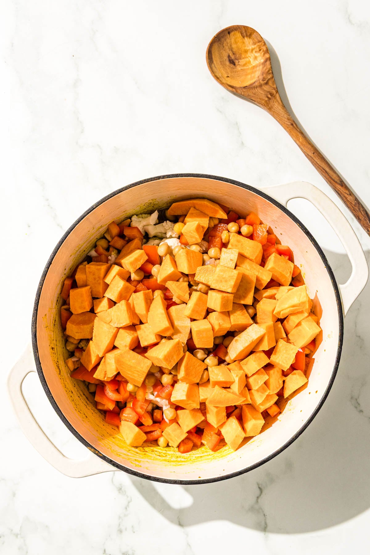 A large pot filled with sweet potato, chickpeas, bell pepper, cauliflower, and diced onion.