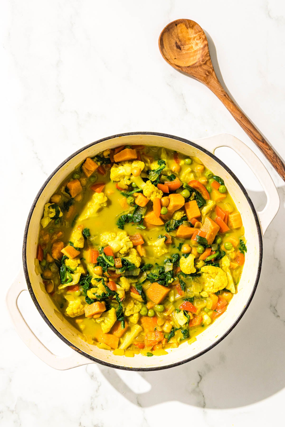 A large pot of sweet potato chickpea curry and a wooden spoon.
