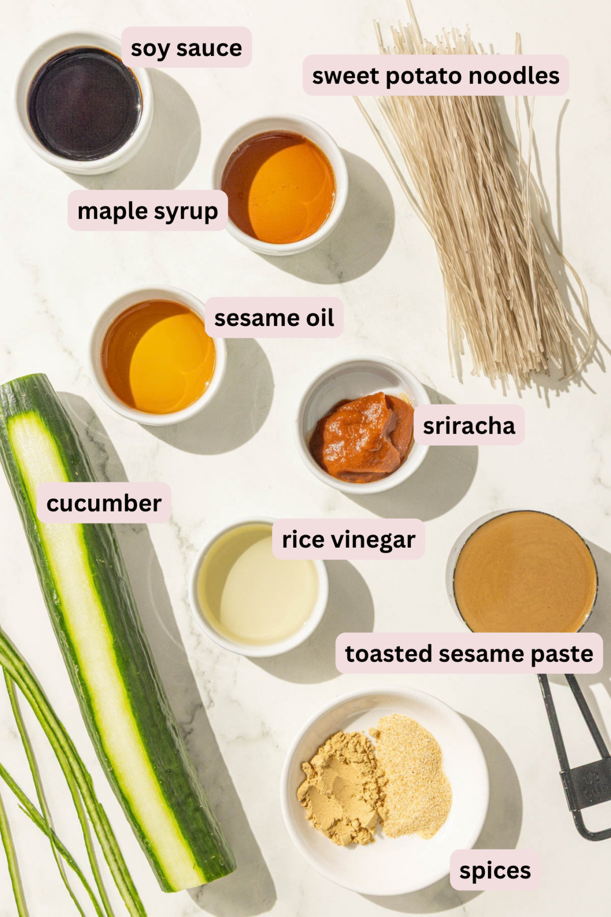 Ingredients laid out in bowls and labeled including soy sauce, sweet potato noodles, maple syrup, sriracha, sesame oil, cucumber, rice vinegar, toasted sesame paste, and spices.