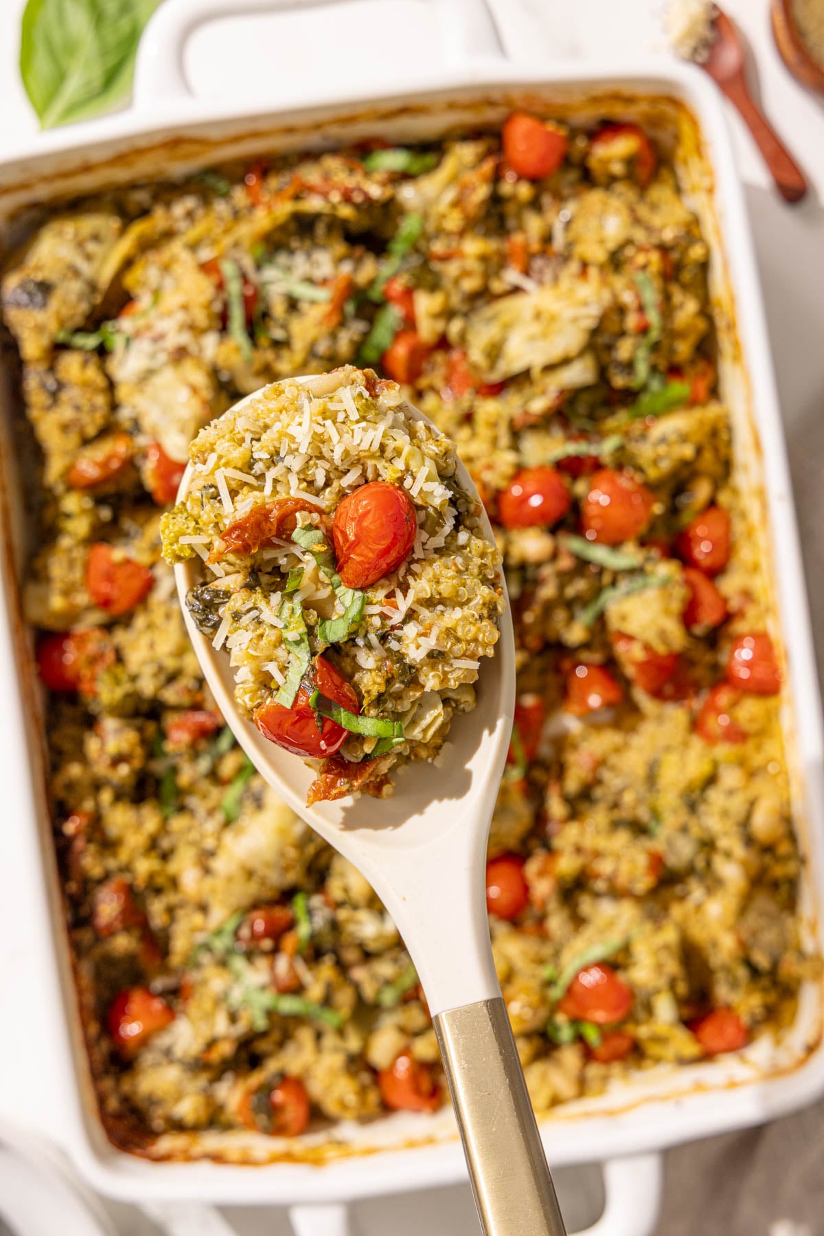 A spoon holding a scoop of pesto quinoa bake over a casserole dish.