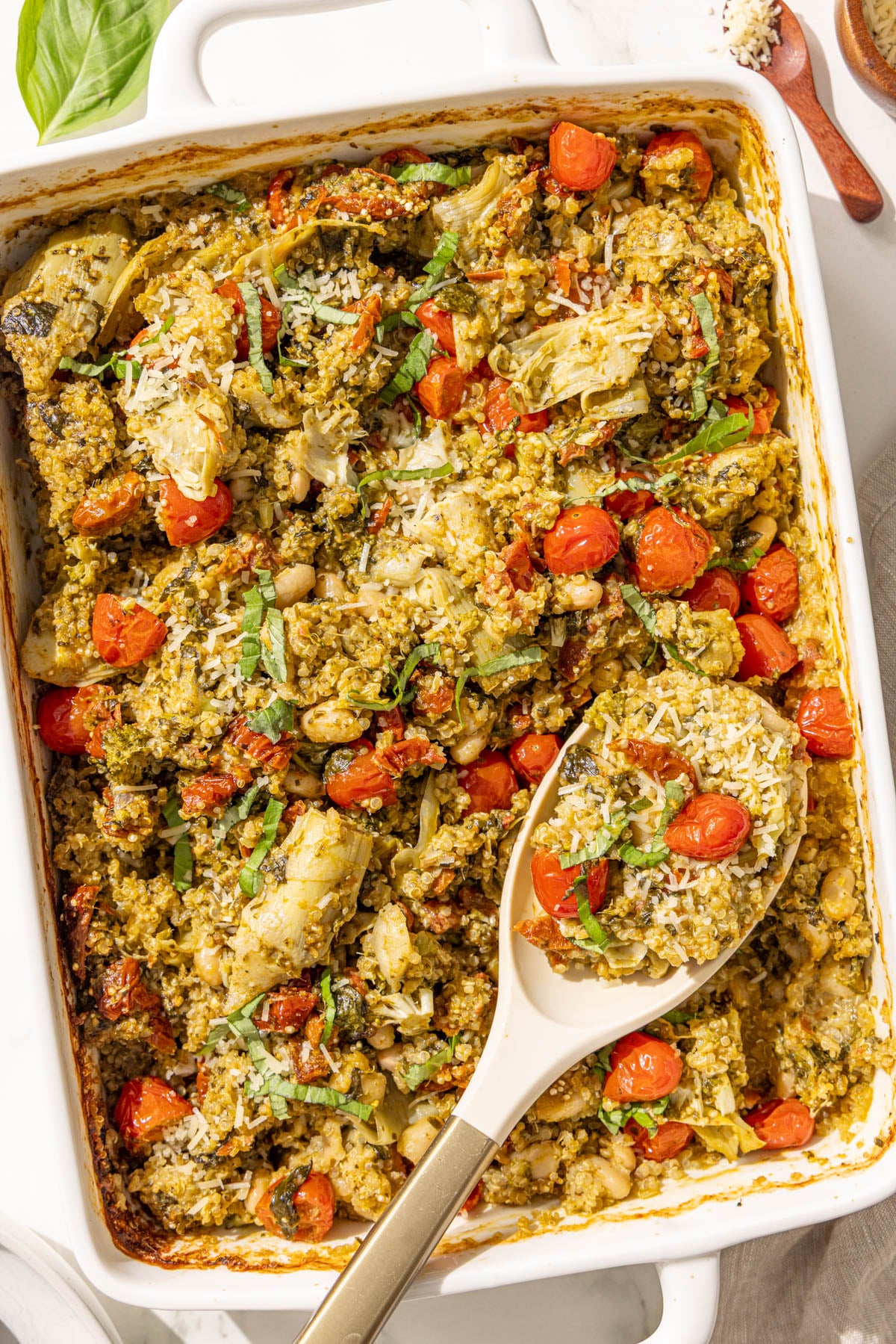 A 9x13 casserole dish of pesto quinoa bake with a spoon in it.