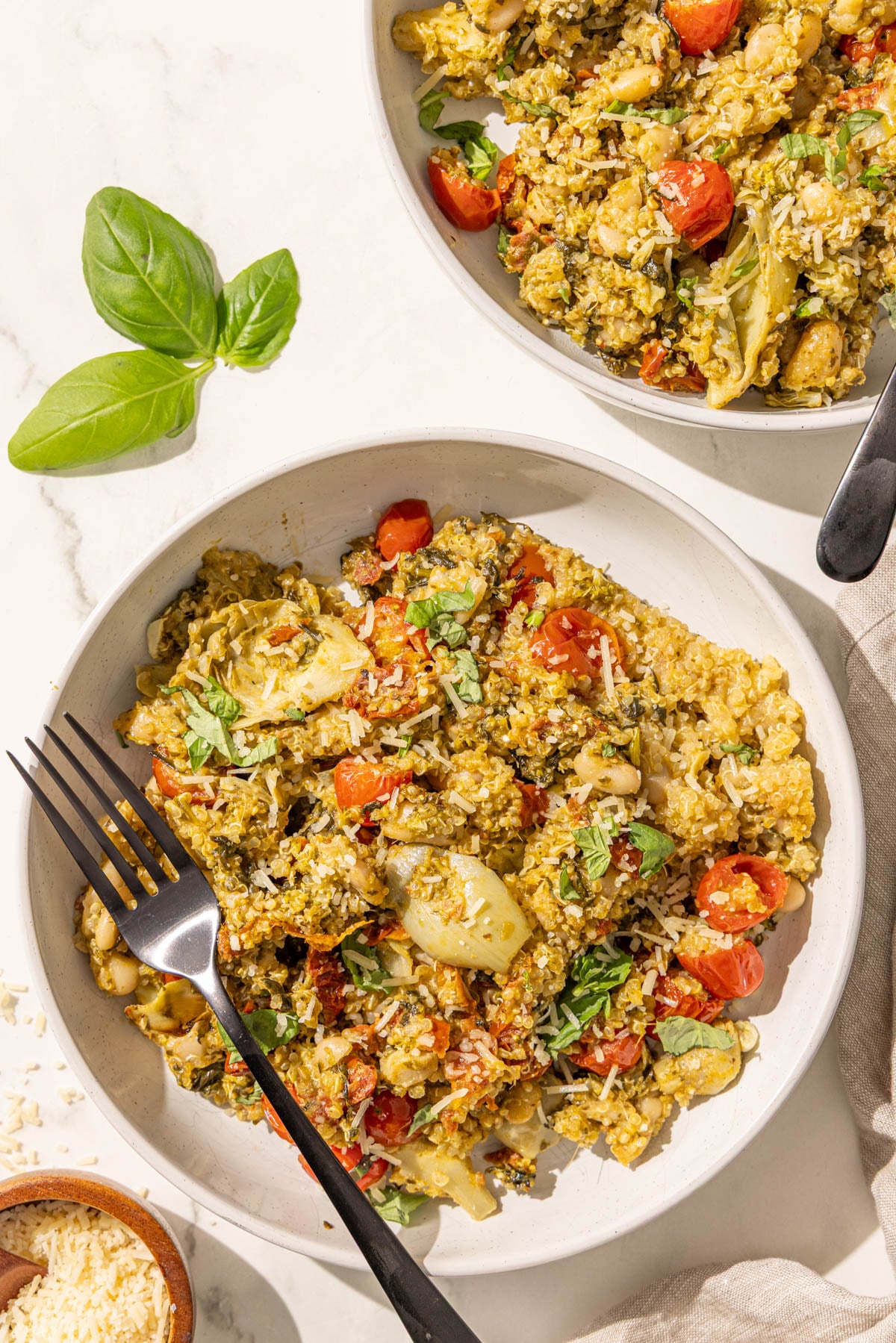 Two bowls of pesto quinoa with black forks in them.
