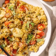 A bowl of pesto quinoa and a black fork in it and a small wooden bowl of parmesan.