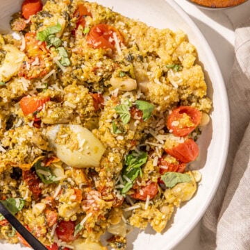 A bowl of pesto quinoa and a black fork in it and a small wooden bowl of parmesan.