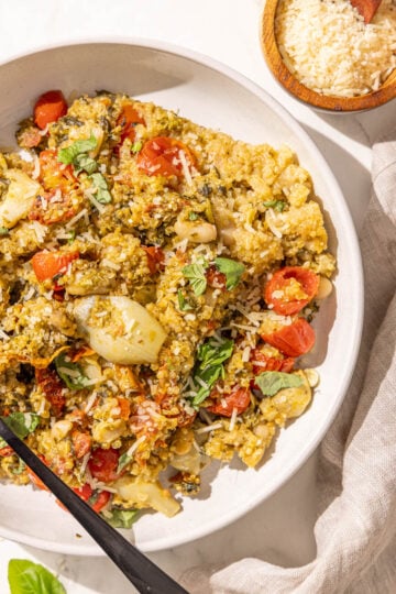 A bowl of pesto quinoa and a black fork in it and a small wooden bowl of parmesan.