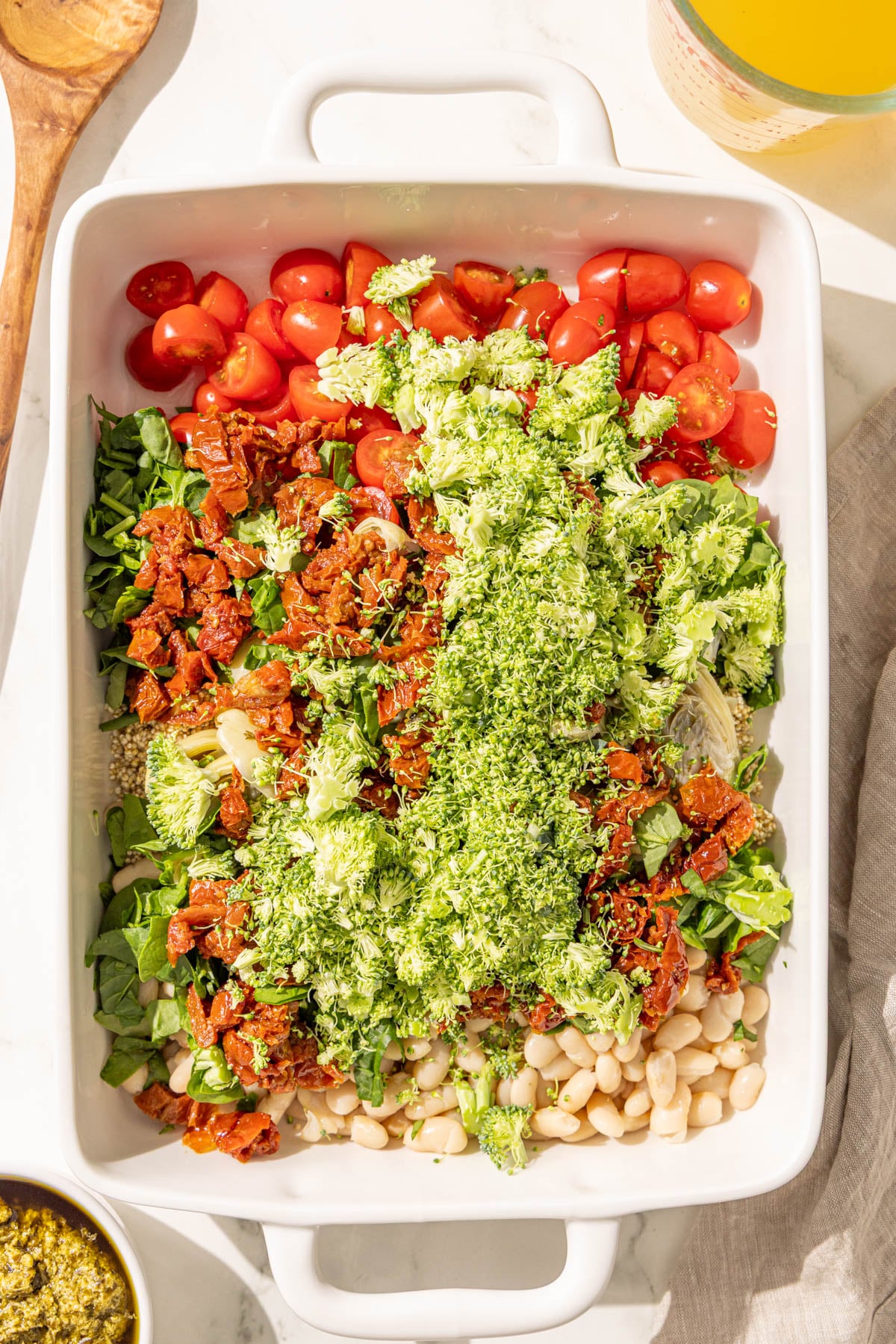 A casserole dish filled with quinoa, white beans, broccoli, tomatoes, spinach, and sun-dried tomatoes.