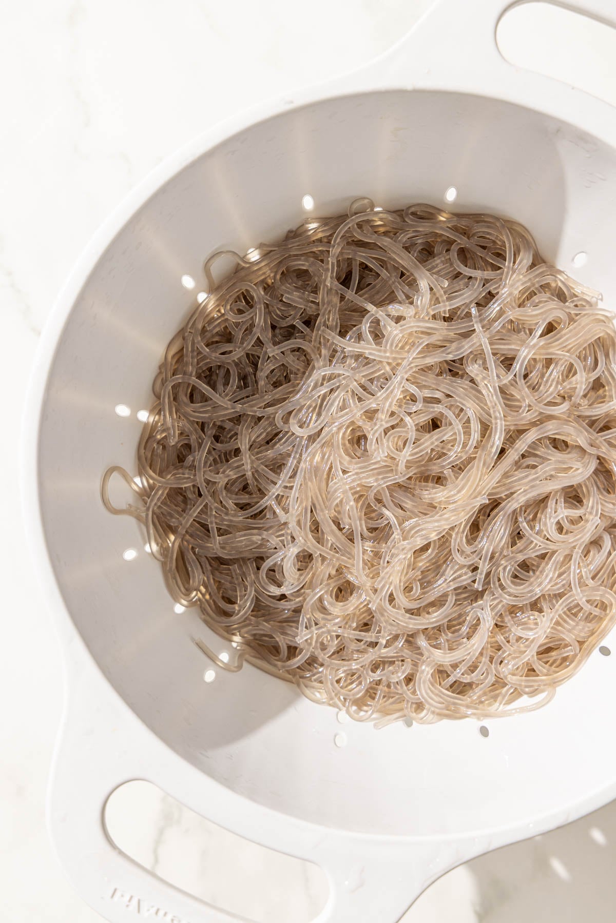 A white strainer filled with cooked glass noodles.