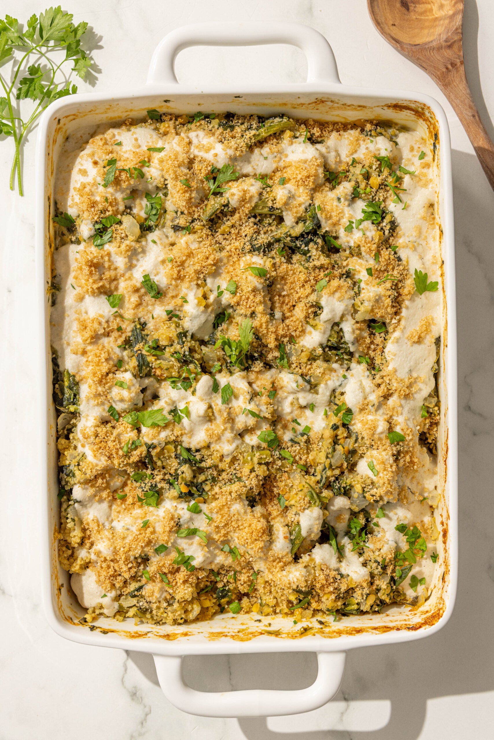 A 9x13 casserole dish with spinach quinoa casserole topped with cashew cream, breadcrumbs, and fresh parsley.