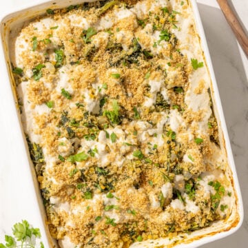 A 9x13 spinach cheesy quinoa casserole topped with parsley and breadcrumbs and a wooden spoon on the counter next to the dish.