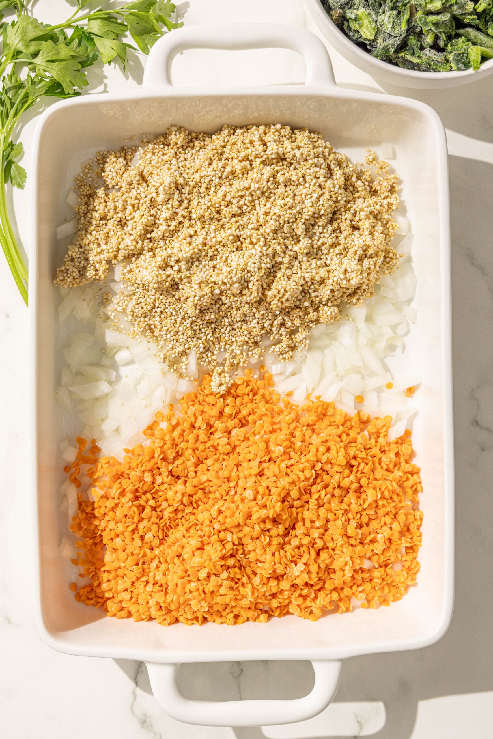 A large glass casserole dish with red lentils, diced onion, and quinoa in it.