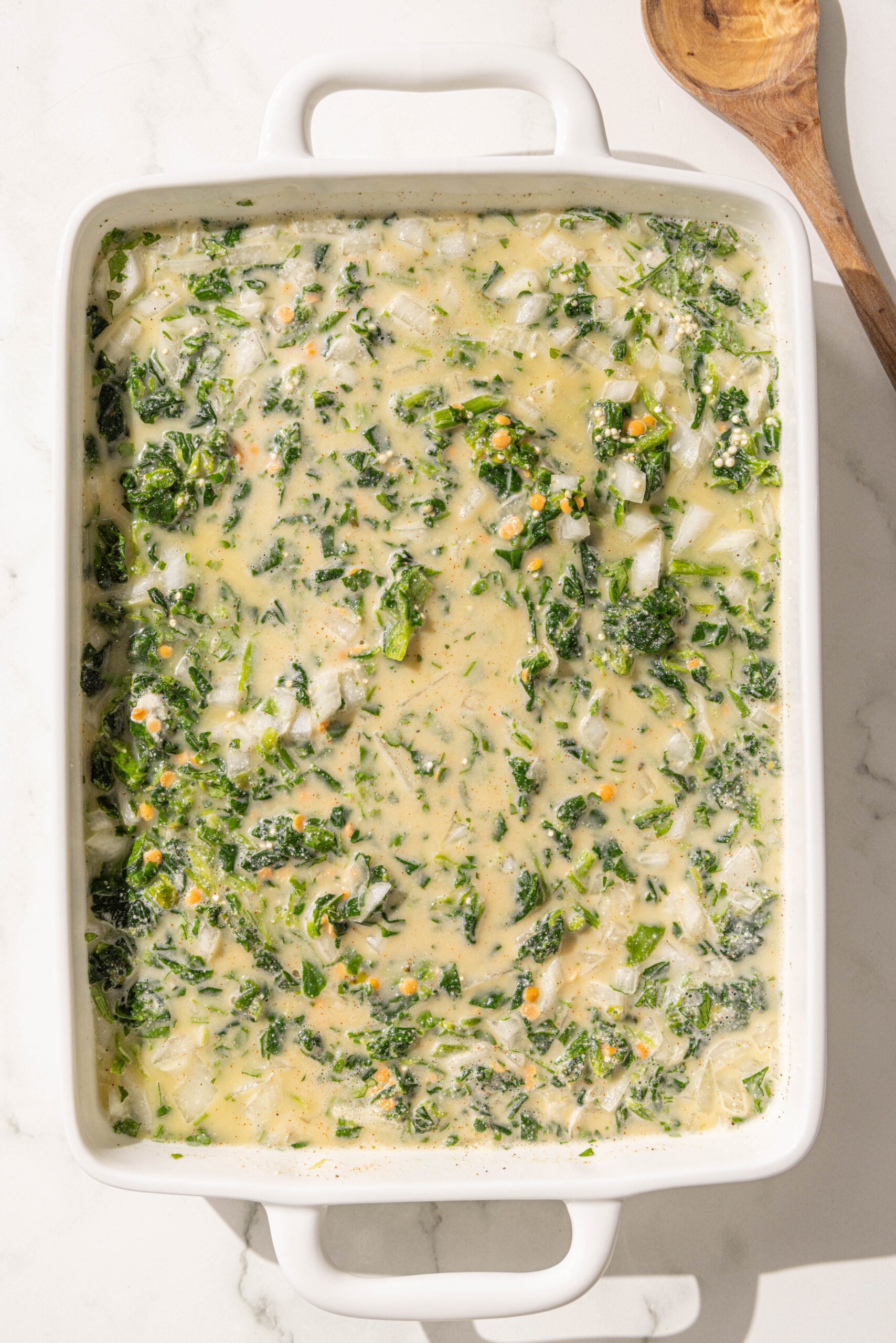 A 9x13 casserole dish with mixed unbaked quinoa spinach casserole.