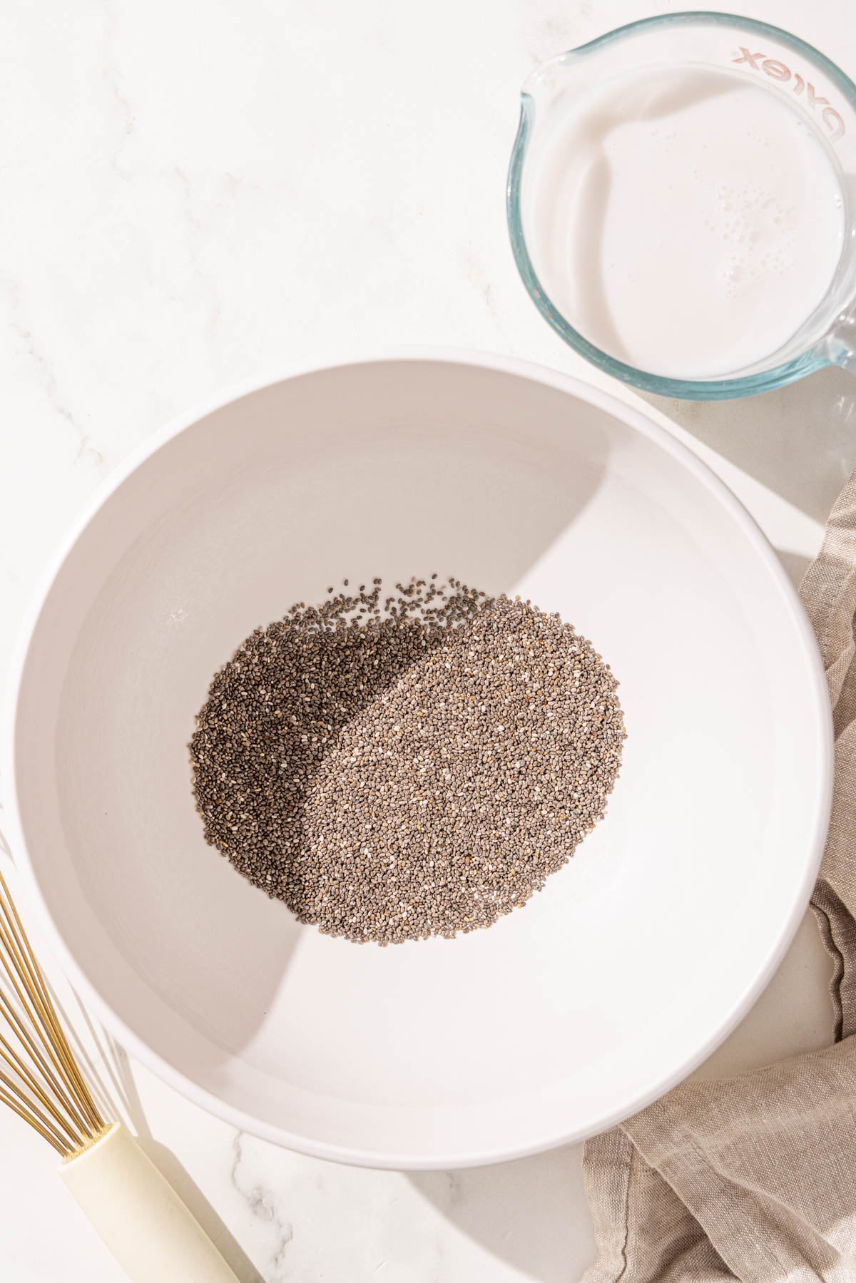 A bowl of chia seeds, a jar of milk, and a whisk.