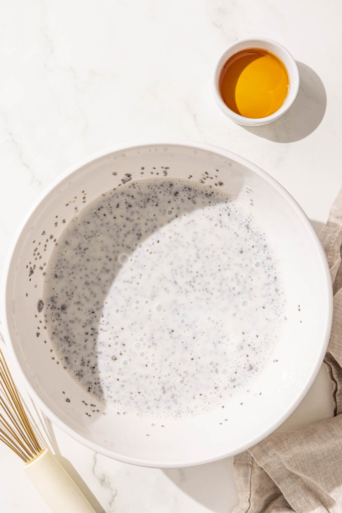 A bowl of chia pudding, a whisk, and a small bowl of maple syrup.