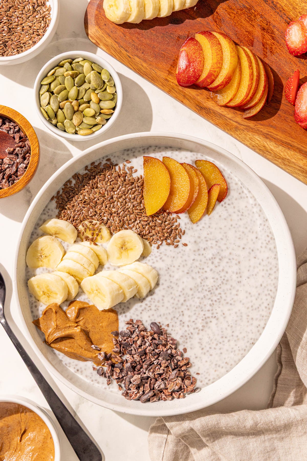 A bowl of chia pudding with banana, almond butter, cacao nibs, flax seed, and plum on it.