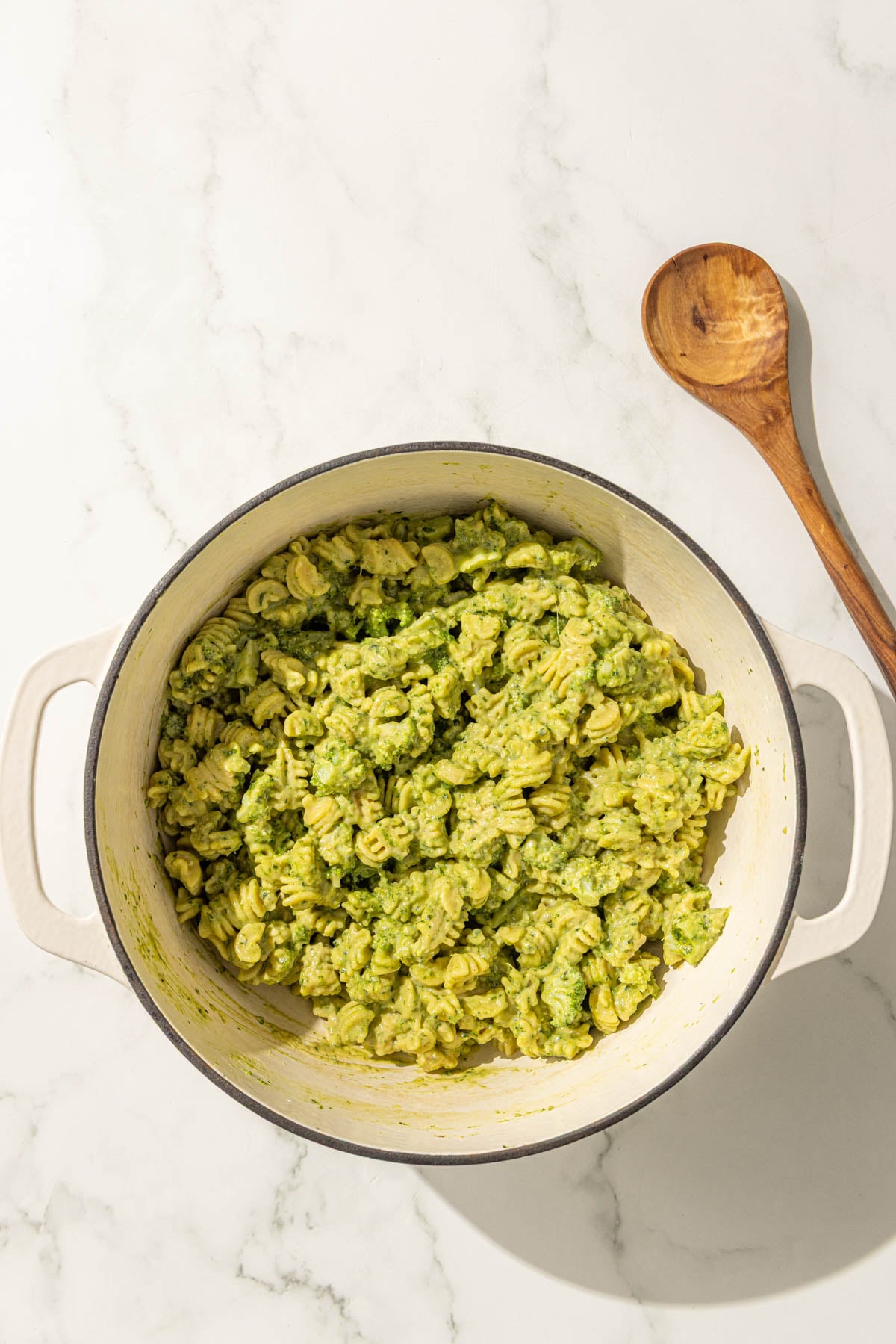 A large pot of pesto hummus broccoli pasta and a wooden spoon.