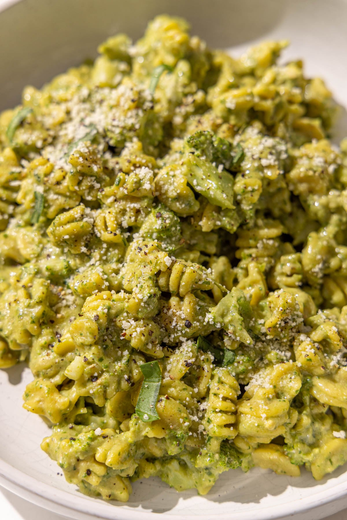 Creamy pesto broccoli hummus pasta in a bowl garnished with fresh basil, parmesan, and black pepper.